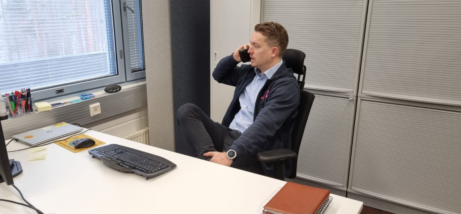 Toimitusjohtaja Juuso Hieta istuu työpöydän ääressä ja puhuu puhelimeen.